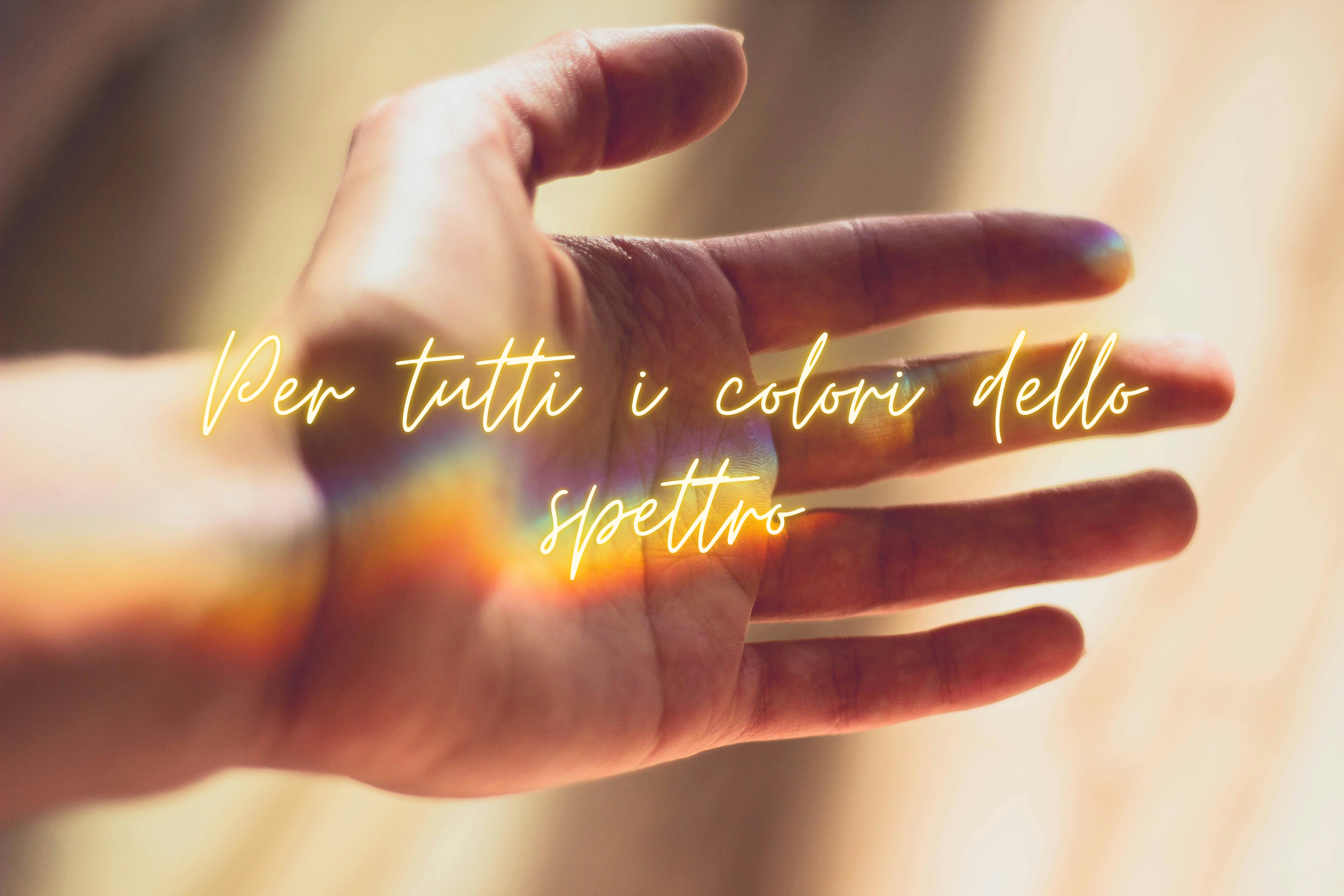 Una arcobaleno è proiettato su una mano aperta. Sulla foto c’è scritto in corsivo: Per tutti i colori dello spettro